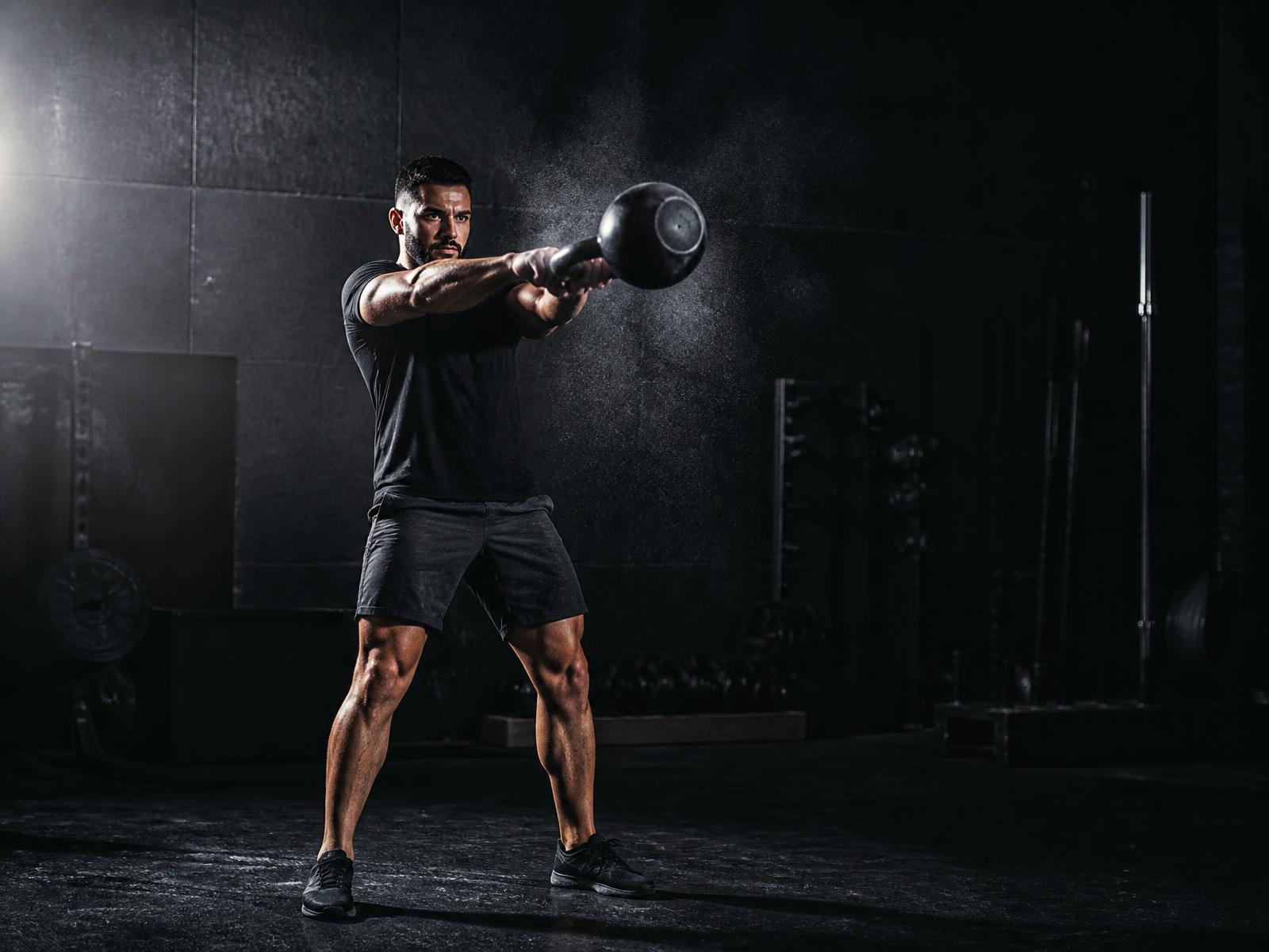Athlete swinging a kettlebell in a dark gym